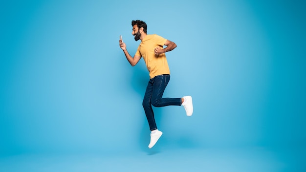 Premium Photo | Overjoyed indian man jumping looking at smartphone and ...