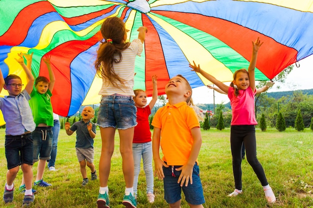 Overjoyed kids bouncing and jumping under rainbow canopy during summer camp outdoors activities