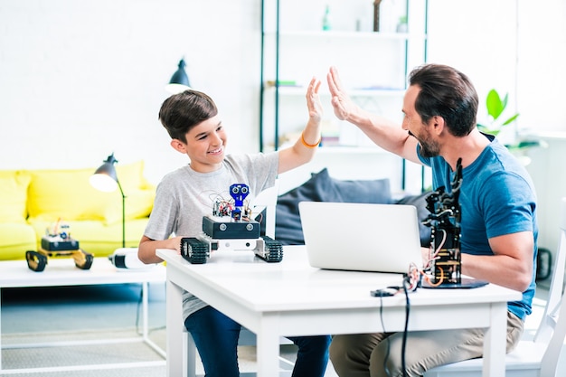Overjoyed little boy giving high five to his father while enjoying engineering practices