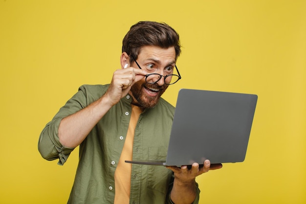 Overjoyed middle aged man looking at laptop screen excited about win or success yellow background