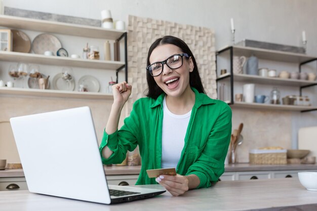 La ragazza millenaria felicissima si siede al tavolo a casa guardando lo schermo del laptop sentendosi euforica vincere online