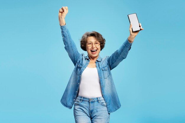 Photo overjoyed senior woman holding mobile phone with mockup celebration success isolated on background