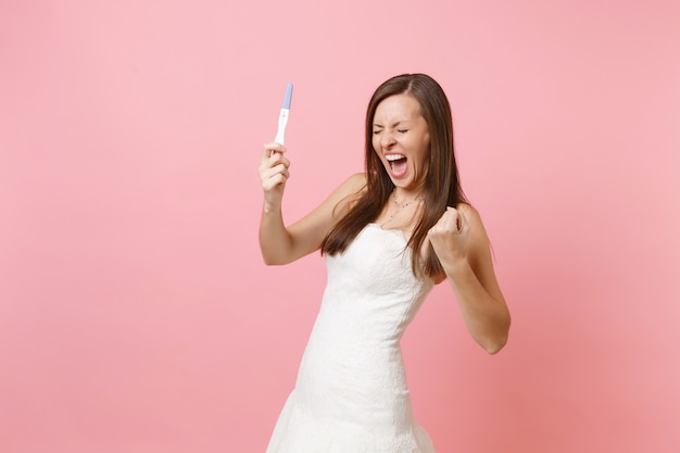 Donna felicissima in abito bianco che urla facendo il gesto del vincitore, tenendo il test di gravidanza pregnancy