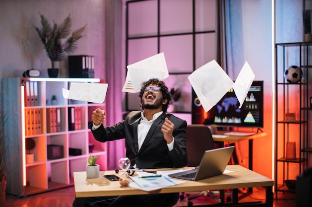 Photo overjoyed young bearded businessman in suit getting good news making good deal throwing papers