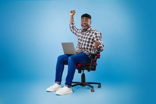 Обрадованный молодой темнокожий мужчина с ноутбуком празднует онлайн-выигрыш или успех в бизнесе