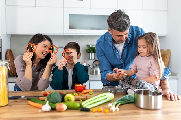Overjoyed young family with son and daughter have fun cooking diner or lunch at home together happy smiling parents enjoy weekend play with small children doing cooking in kitchen