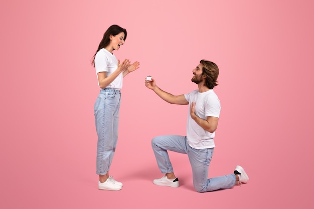 Overjoyed young woman reacts with surprise as man kneels with an engagement ring