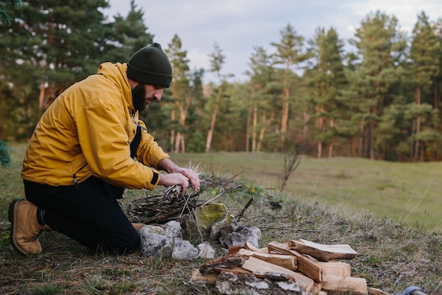 Overleven in het wild Een man met een baard steekt een vuur aan bij een geïmproviseerde schuilplaats gemaakt van dennentakken