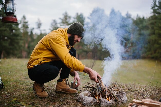 Overleven in het wild Een man met een baard steekt een vuur aan bij een geïmproviseerde schuilplaats gemaakt van dennentakken