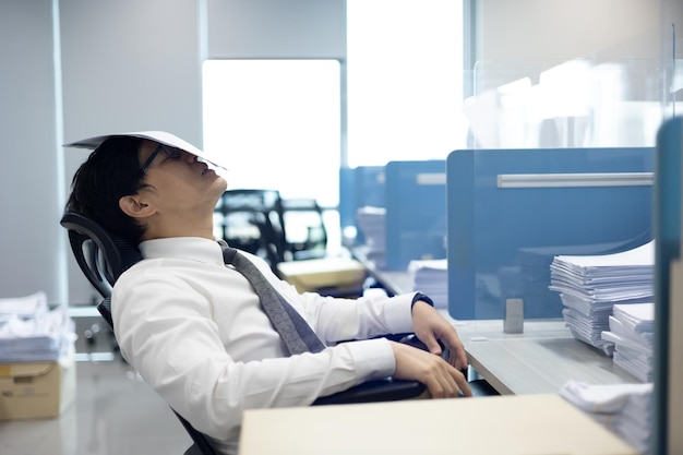 Overload office worker Asian office worker is feel headache and stressed sitting at desk and put paperwork on face at the office