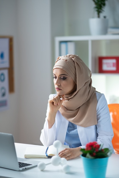 Overloaded with work. Female chemist wearing headscarf feeling overloaded with work after checking schedule