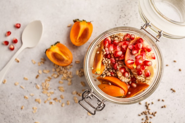 Overnight oatmeal with pomegranate, persimmon and hemp seeds, white background.