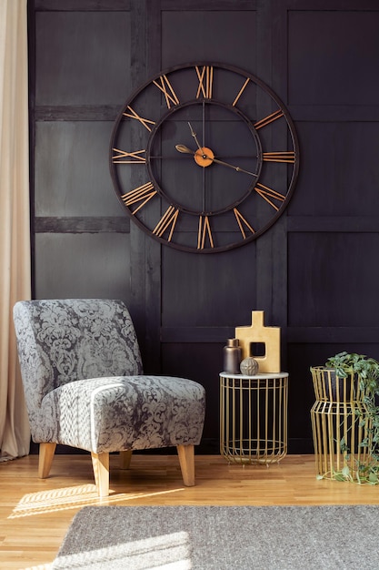 Oversized wall clock armchair and golden table with a vase in a living room interior Real photo