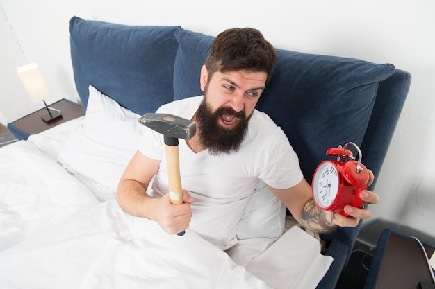 Overslept again tips for waking up early tips for becoming an\
early riser man bearded hipster sleepy face in bed with alarm clock\
problem with early morning awakening get up with alarm clock