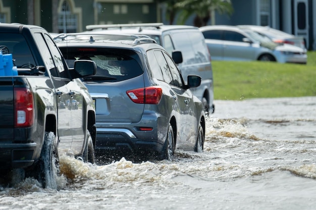 Overstroomde stadsstraat met rijdende auto's onder water in een woonwijk in Florida na de landing van orkaan Ian Gevallen van een natuurramp