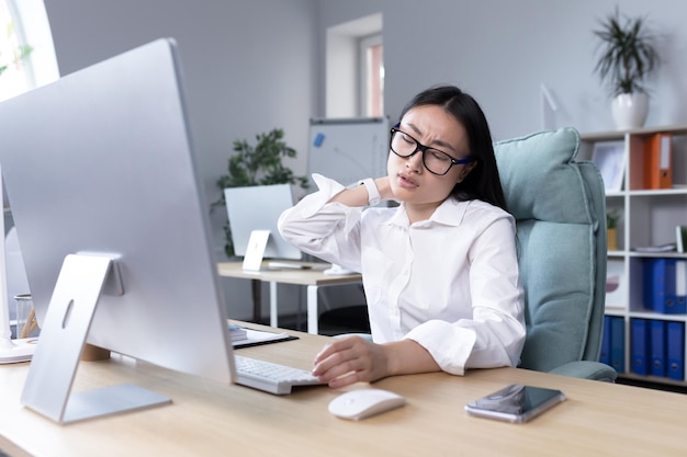 Overtired asian woman office worker has severe neck pain massages neck muscles with hand female