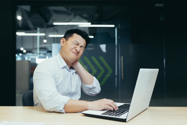 Overtired asian worker in office having severe neck pain