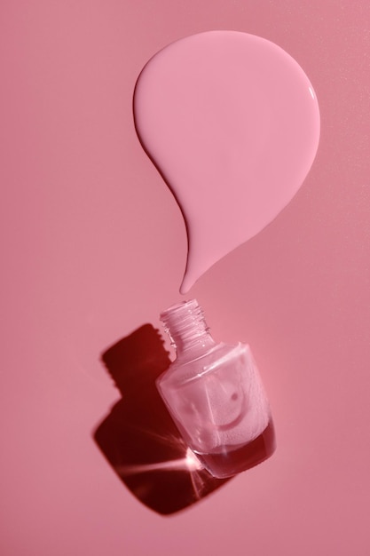 Overturned bottle with pink nail polish on a pink background