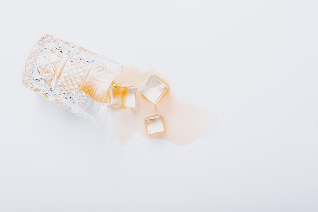 Overturned glass with whiskey on a white background ice cubes fell out of a glass