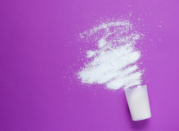 The overturned measuring capacity of scattered powder on purple table. Top view