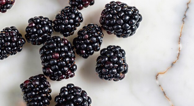 Overturned mug with blackberries on white marble table closeup