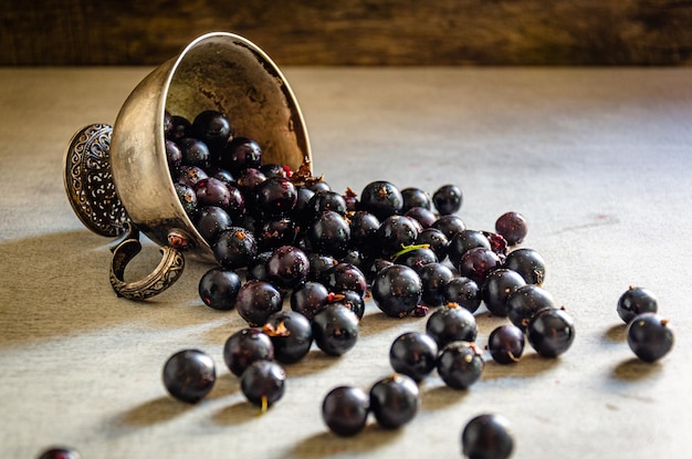 An overturned silver cup with blackcurrants on the table.