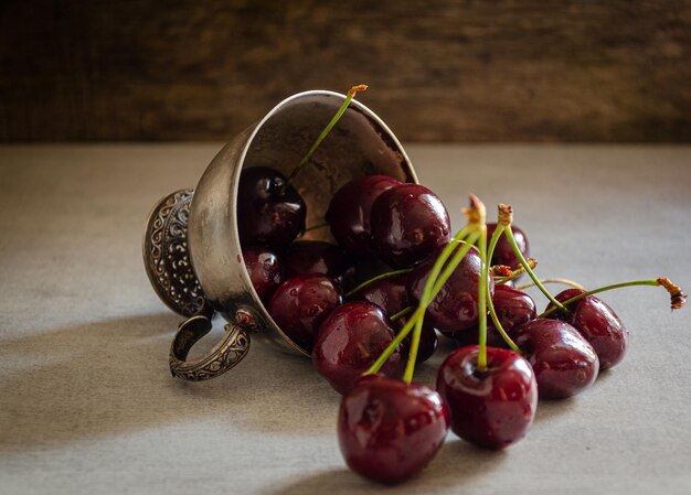 An overturned silver cup with ripe cherries is on the table.