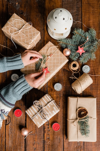 Overview of young woman hands making knot on top of packed and wrapped giftbox while preparing gifts for Christmas