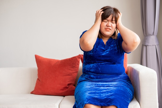 An overweight Asian woman is sitting on the sofa in the living room.