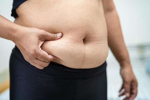 肥満のアジア人女性がオフィスで太った腹を示す