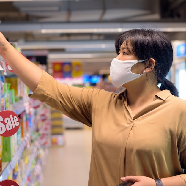슈퍼마켓 내부 코로나 바이러스 발생 쇼핑으로부터 보호하기 위해 마스크와 중량이 초과 된 아시아 여자