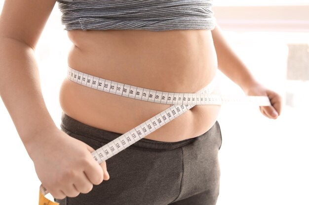 Overweight boy measuring his waist at home closeup