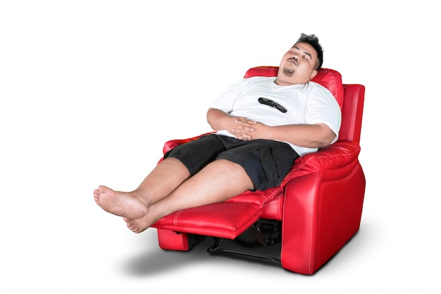 Photo overweight lazy man with remote control napping on sofa against white background