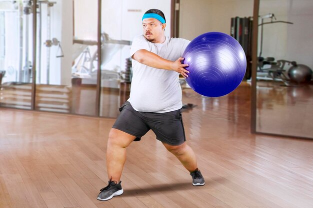 Overweight Man doing fitness exercise on pilates ball at a gym