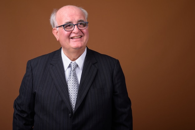 Overweight senior businessman wearing eyeglasses against brown wall