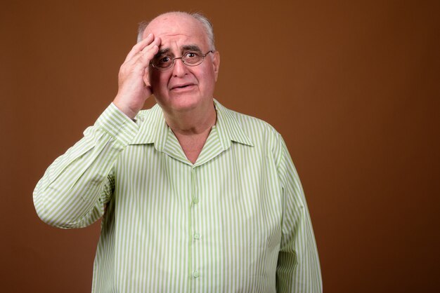 Overweight senior man wearing eyeglasses against brown wall