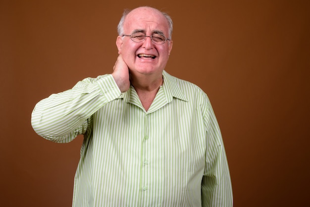 Overweight senior man wearing eyeglasses against brown wall