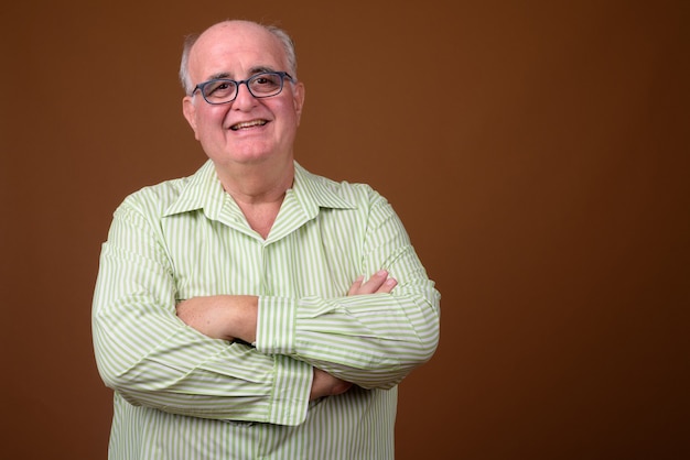 Overweight senior man wearing eyeglasses against brown wall