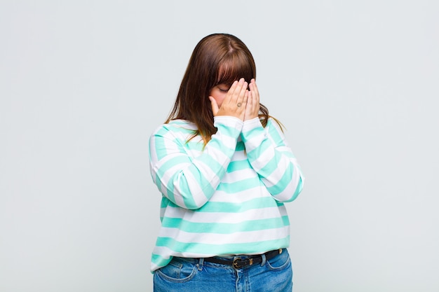Overweight woman covering eyes with hands with a sad, frustrated look of despair, crying, side view