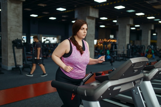 Overweight woman doing exercise on treadmill in gym, active training. Obese female person struggles with excess weight, aerobic workout against obesity, sport club