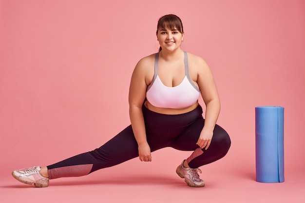 Overweight woman doing fitness exercise, body positive, pink wall