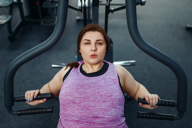 Overweight woman on exercise machine in gym, top view, active training