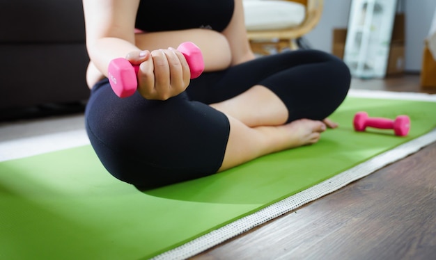 太りすぎの女性は、居間で自宅でストレッチ位置でダンベルを使用して減量運動のために運動します 陽気な太った女性の食事療法の健康的なライフ スタイルのコンセプト