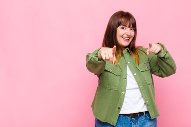 Overweight woman feeling happy and confident, pointing with both hands and laughing, choosing you