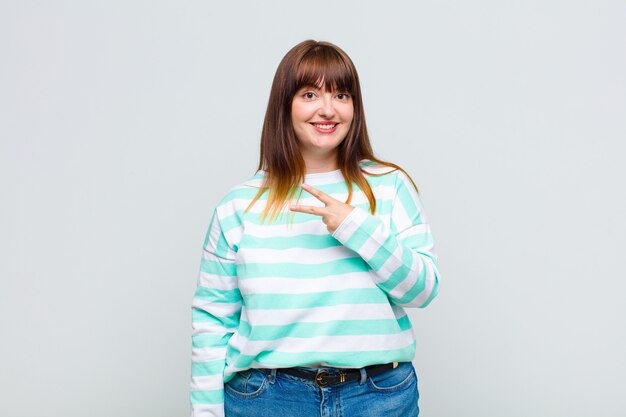 Overweight woman feeling happy, positive and successful, with hand making v shape over chest, showing victory or peace