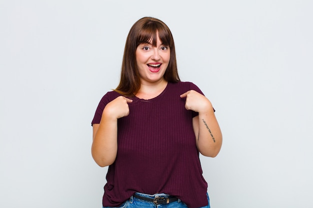 Overweight woman feeling happy, surprised and proud, pointing to self with an excited, amazed look