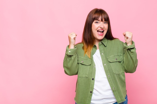 Overweight woman feeling happy, surprised and proud, shouting and celebrating success with a big smile