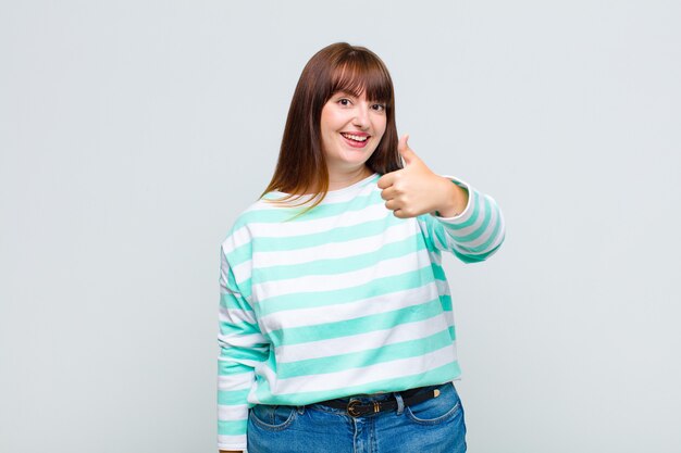 Overweight woman feeling proud, carefree, confident and happy, smiling positively with thumbs up