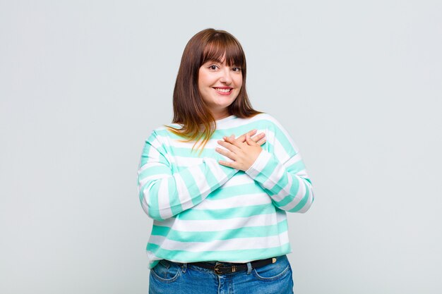 Overweight woman feeling romantic, happy and in love, smiling cheerfully and holding hands close to heart