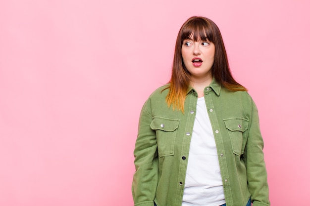 Photo overweight woman feeling shocked, happy, amazed and surprised, looking to the side with open mouth